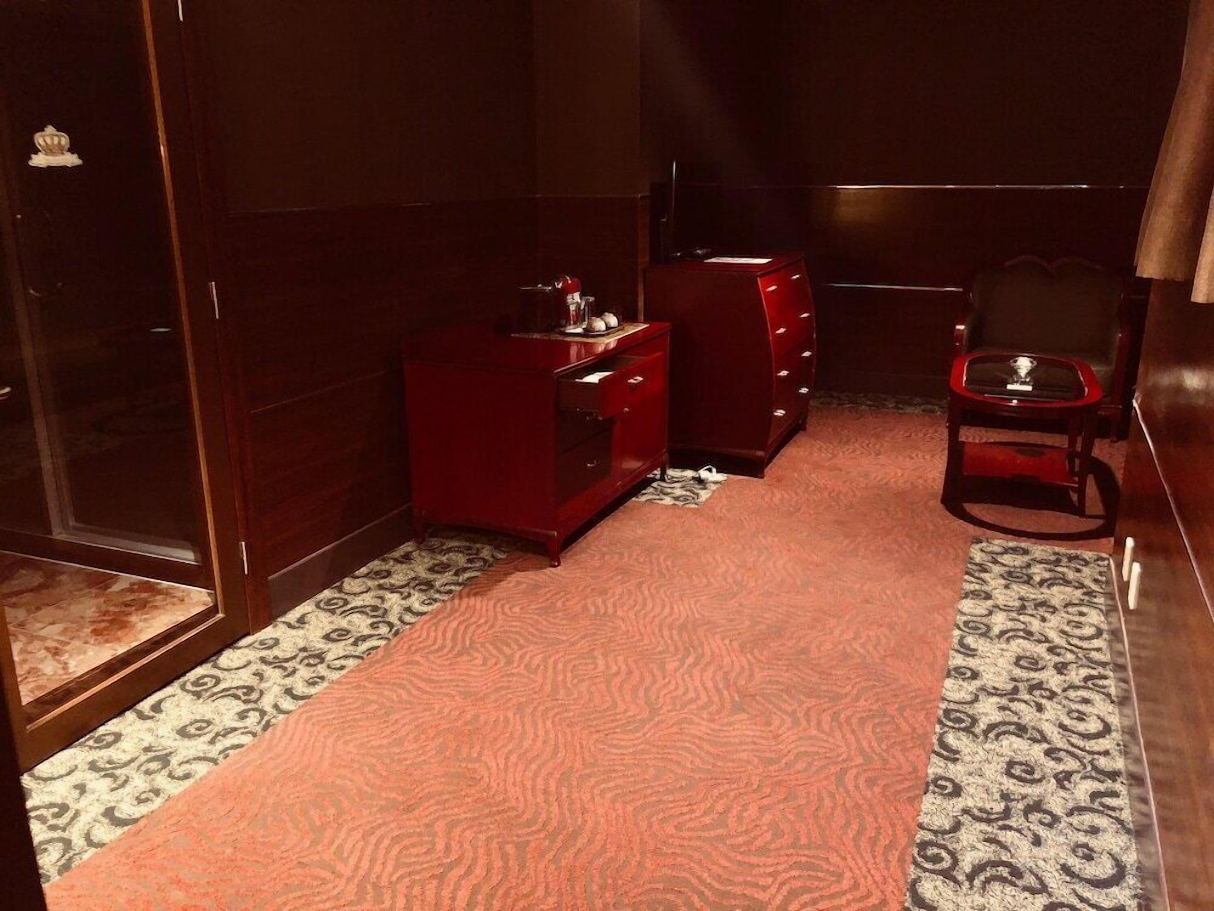 Una habitación con alfombra estampada, un aparador rojo, una silla y una puerta de madera.