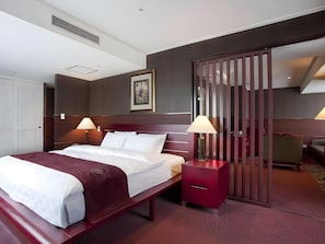 Habitación de hotel con una cama grande, dos lámparas de noche, un cabecero de madera, una mesita de noche roja, un armario y una puerta corredera.