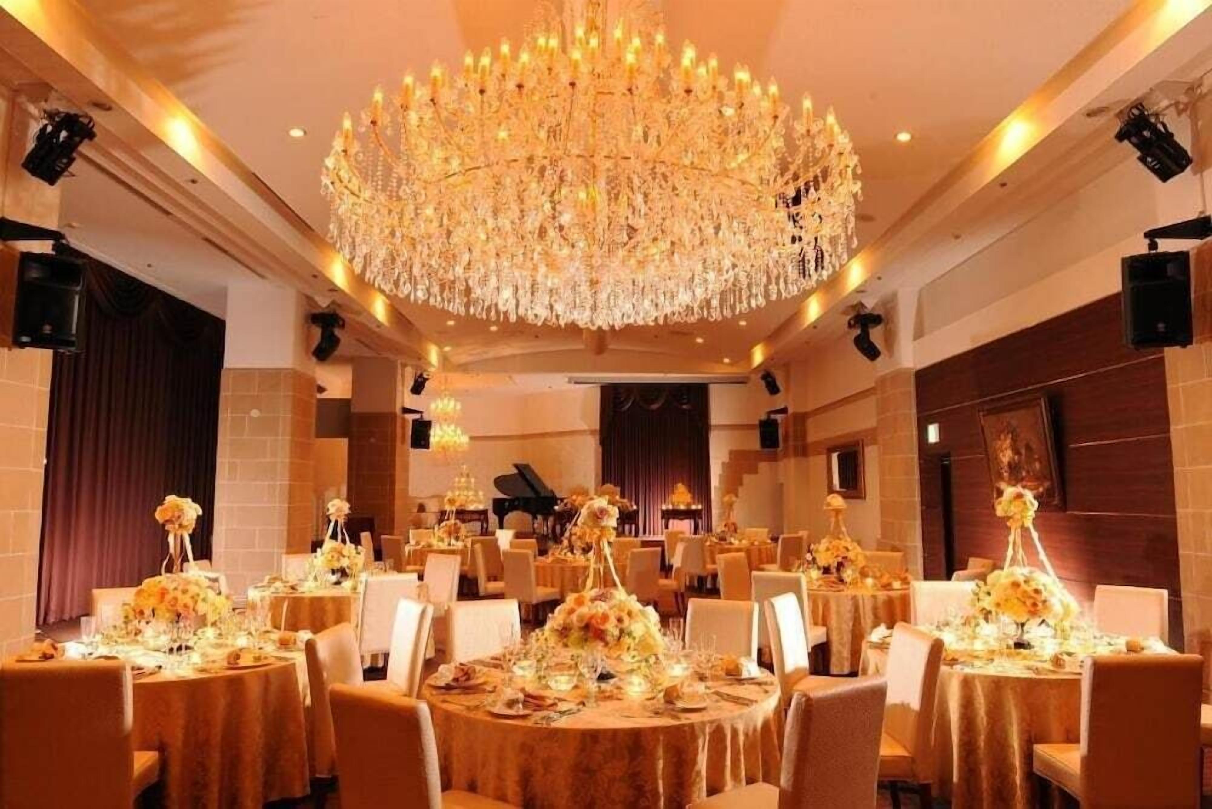 A banquet hall with round tables, a large chandelier, and a grand piano.