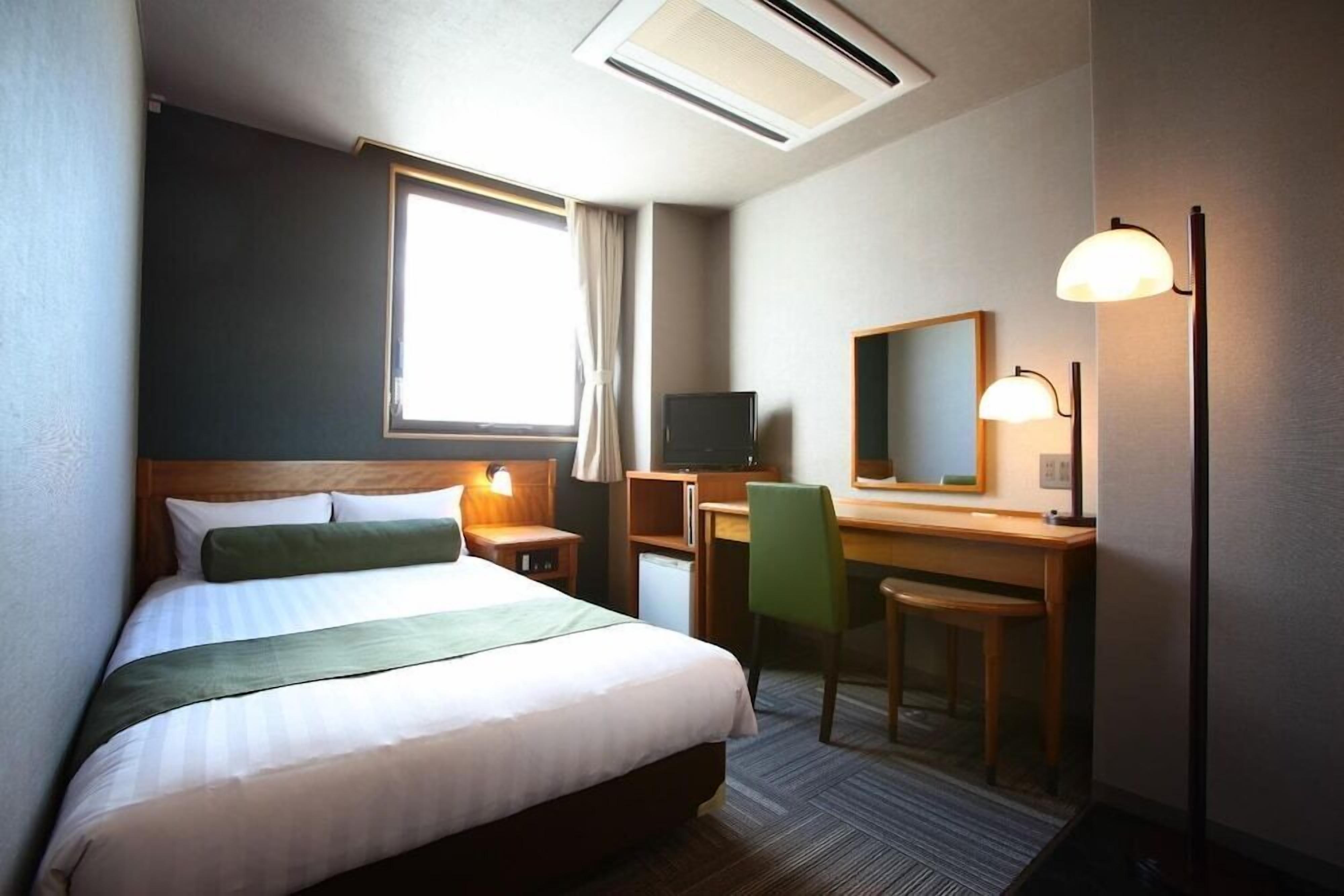 Une chambre d’hôtel avec un lit, un bureau, une chaise, une télévision et un miroir.