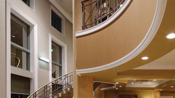 Un amplio hall con una escalera curva, ventanas grandes y una zona de estar con sillas y mesas.