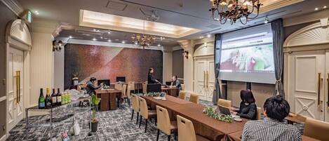 Una sala conferenze con un grande schermo, diversi tavoli e sedie, dotata di portatili e un proiettore.