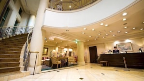 Un vestíbulo de hotel con una escalera curva, un mostrador de recepción y un área de descanso con sillas y mesas.