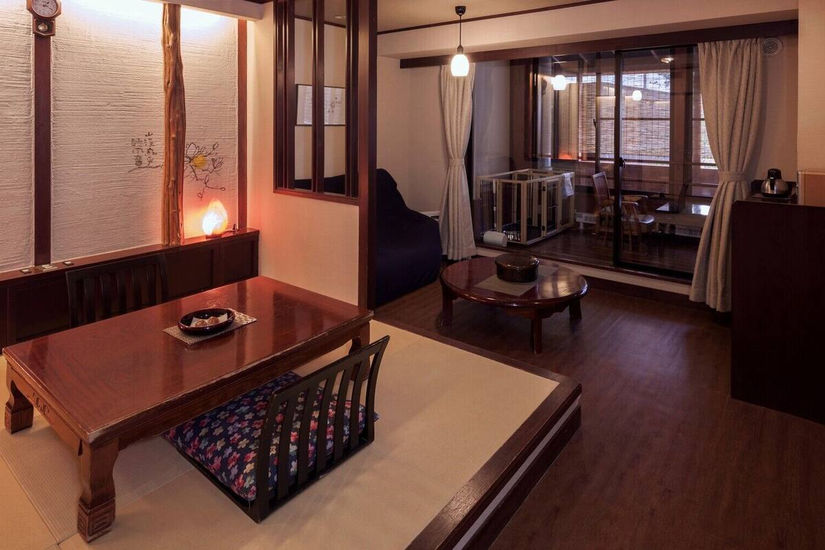 A traditional Japanese-style room with tatami flooring, a low table with a cushion, a sofa, and a television.