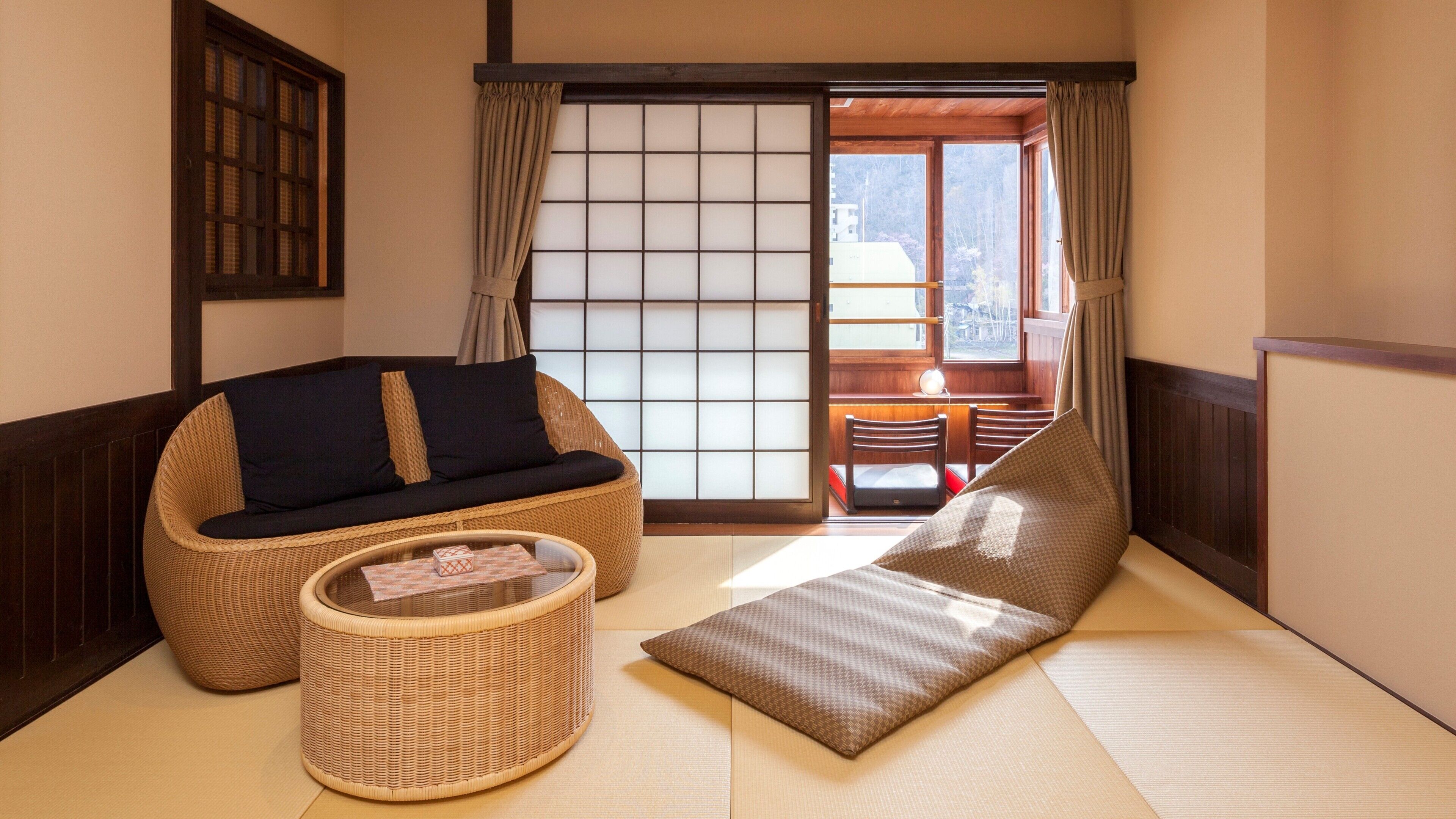 Perinteinen japanilaistyylinen huone, jossa on tatamimatto, matala pöytä ja pehmuste, punottu tuoli sekä liukuovi, josta on näkymä ulos.