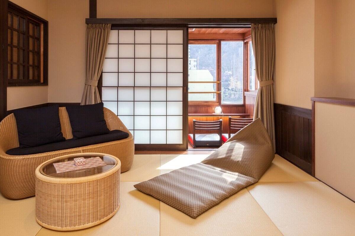 A traditional Japanese room with tatami flooring, a low table, a sofa, and a window with shoji screens.