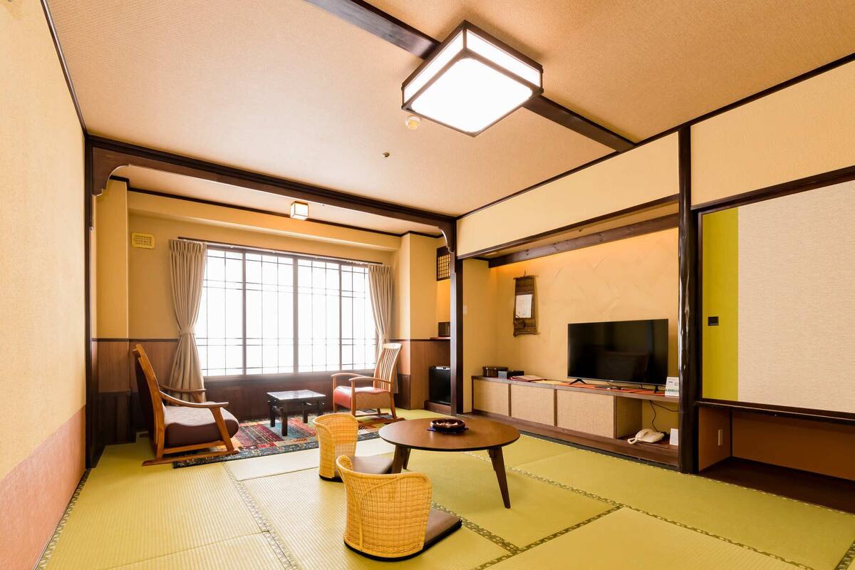 A traditional Japanese-style room with tatami flooring, a low table, chairs, a television, and a sliding door.