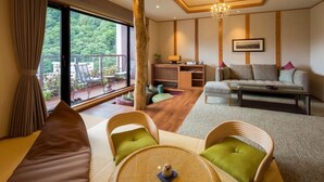 A modern living room with a sofa, chairs, a coffee table, and a desk with a lamp. There is a large window with a view of greenery outside. - Nukumori no Yado Furukawa (Sapporo)