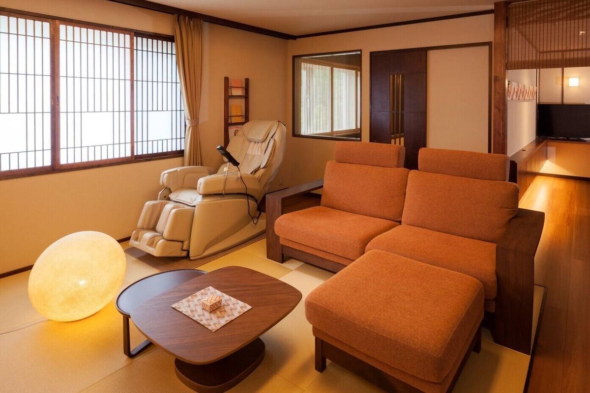 A room with a massage chair, a sofa, a TV, and a bed.