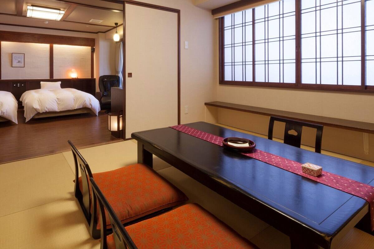 A traditional Japanese-style room with tatami flooring, a low table with a red mat, and two beds with white bedding.