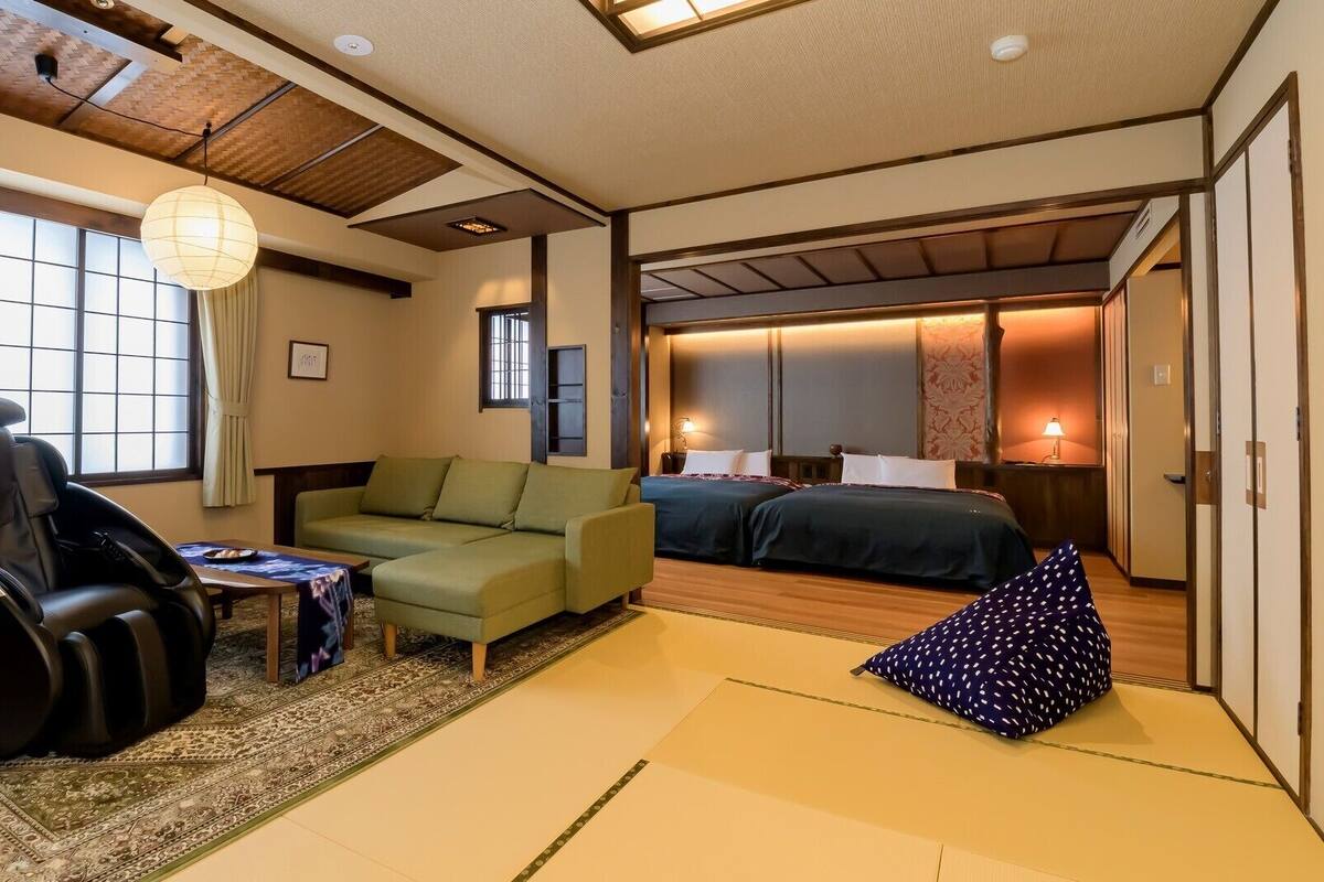 A traditional Japanese-style room with tatami flooring, a futon bed, a massage chair, and a low table with a small tablecloth.