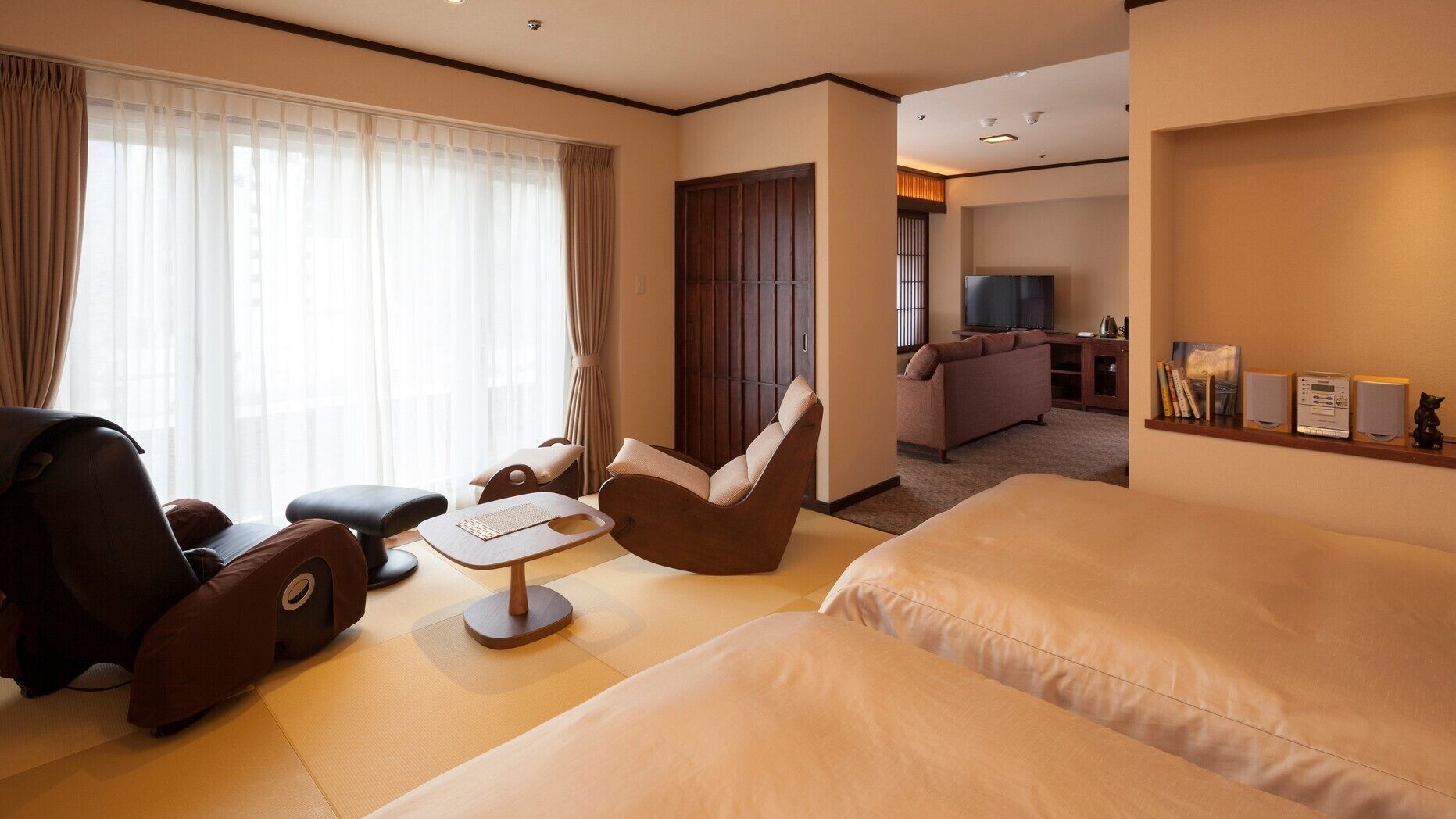 Une chambre d’hôtel avec un canapé, une chaise, une petite table et un téléviseur en arrière-plan.