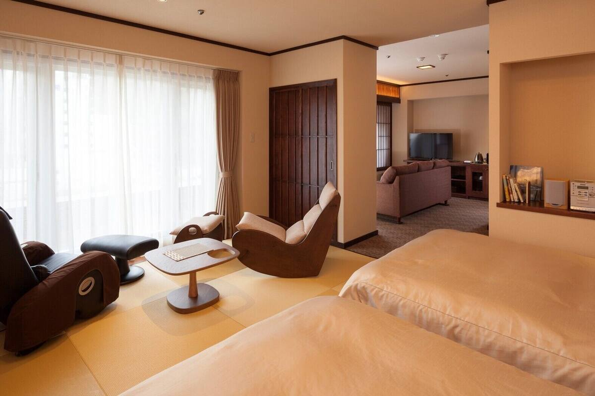 A hotel room with a sofa, a chair, a small table, and a TV in the background.