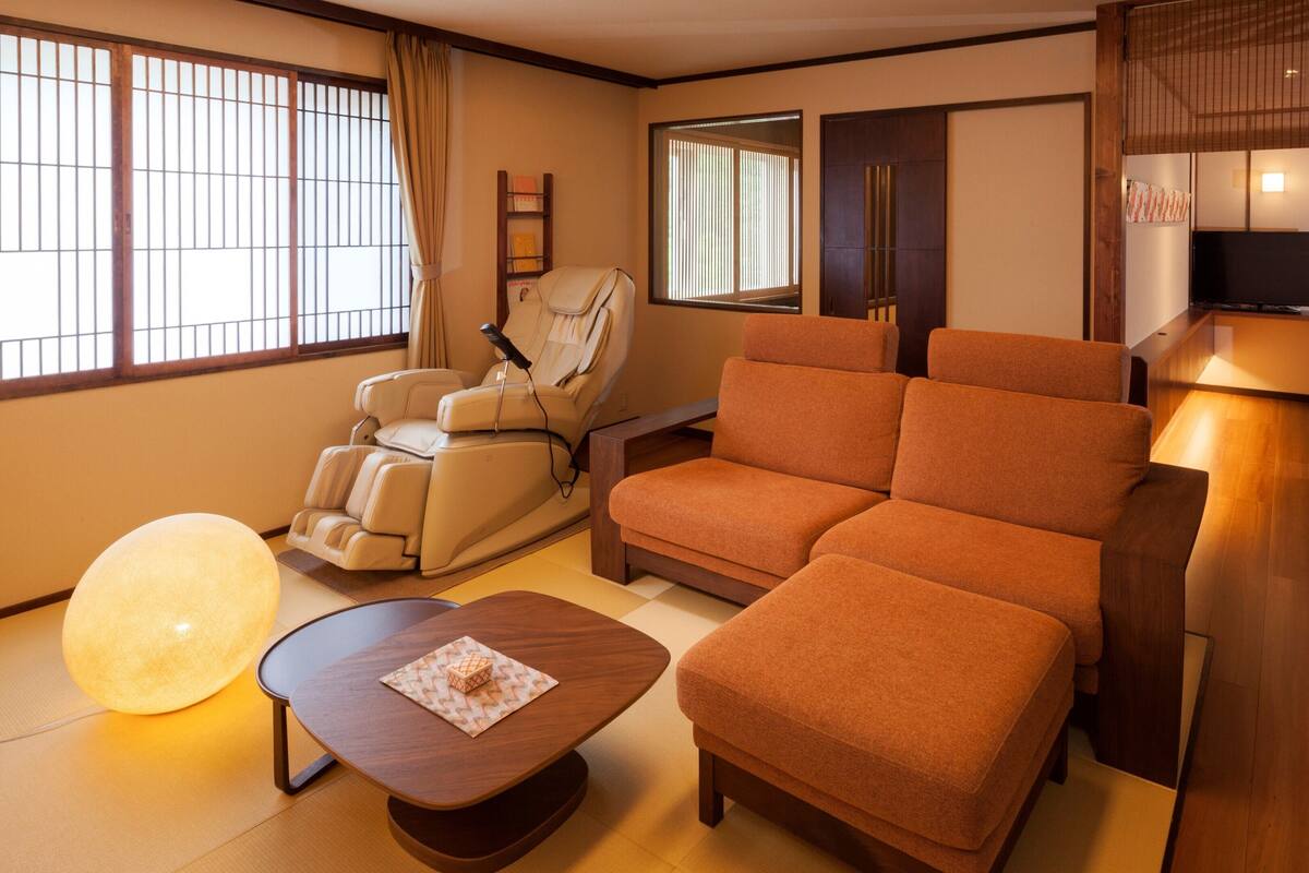 A room with a massage chair, a sofa, a TV, and a bed.
