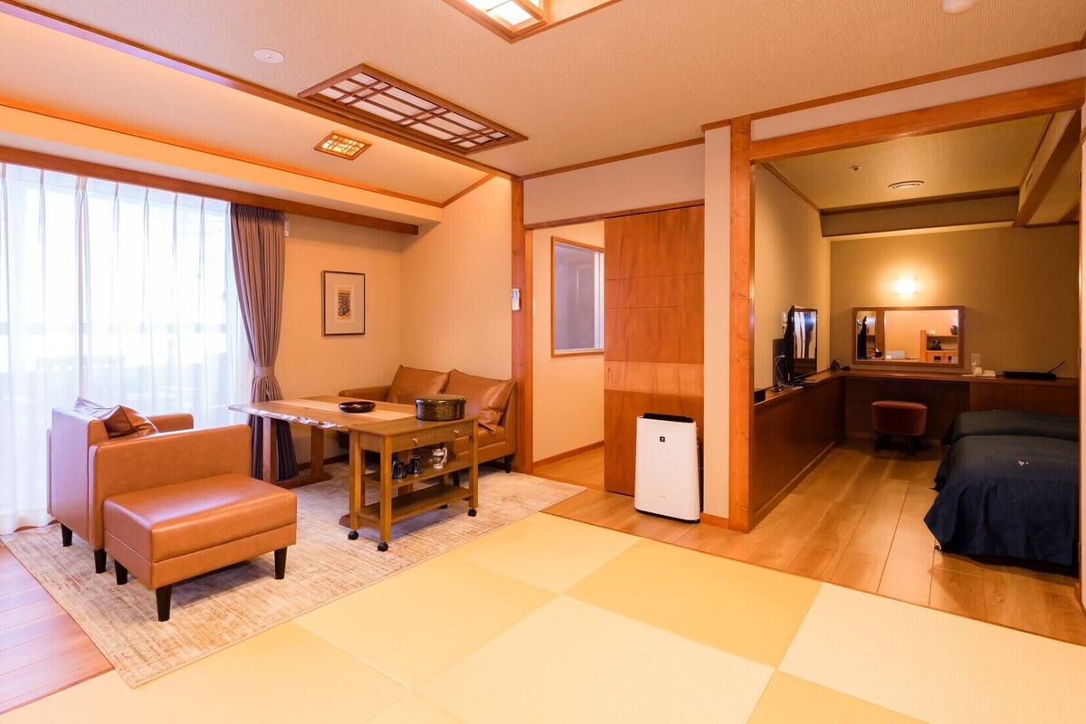 A hotel room with a sofa, a small table, a desk, a bed, and a kitchenette.
