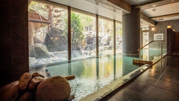 A spa area with a hot tub, a view of a rocky outdoor landscape, and a tiled floor. - Nukumori no Yado Furukawa (Sapporo)