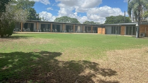 A building with a covered outdoor seating area, a grassy lawn, and a clear sky. - Jumbuck Motel (Longreach)