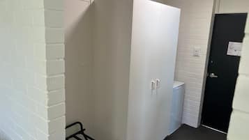 Un pasillo estrecho con una pared de ladrillo blanco, una puerta blanca y un armario blanco.