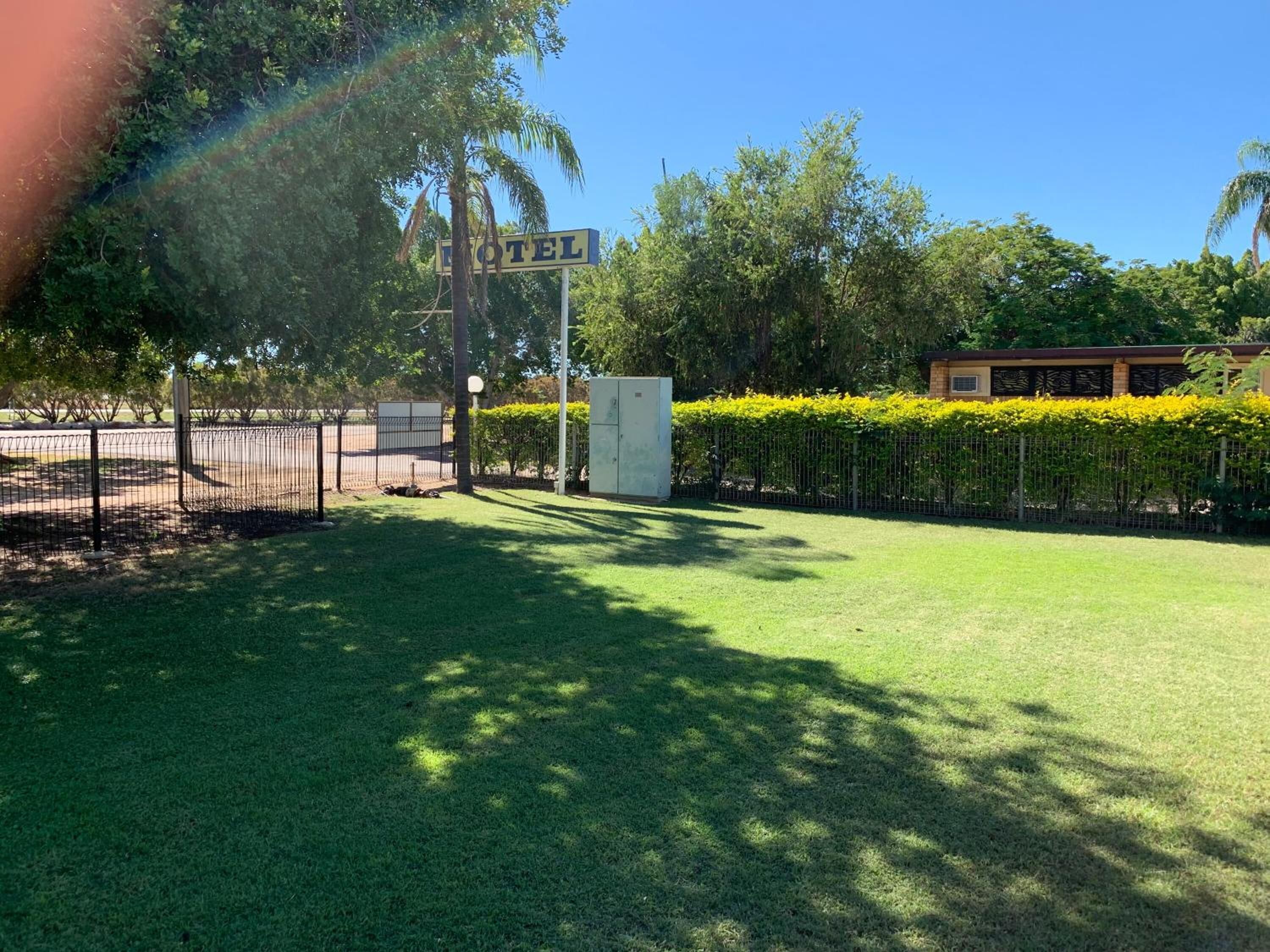 A hotel entrance with a sign, a fenced parking area, and a well-maintained lawn.