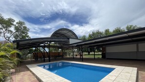 A swimming pool with a tiled deck, a covered patio area, and a brick wall. - Jumbuck Motel (Longreach)