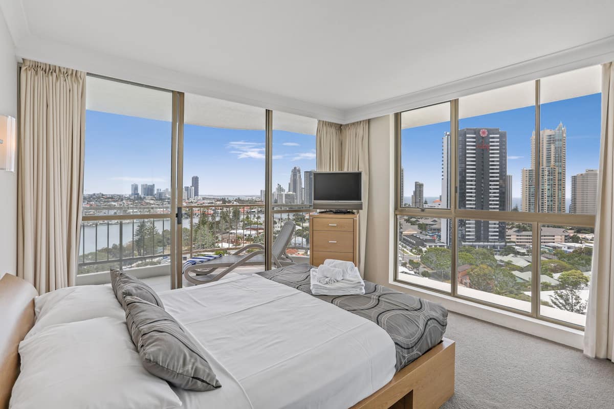 Habitación de hotel con una cama grande, televisión y vista a la ciudad.