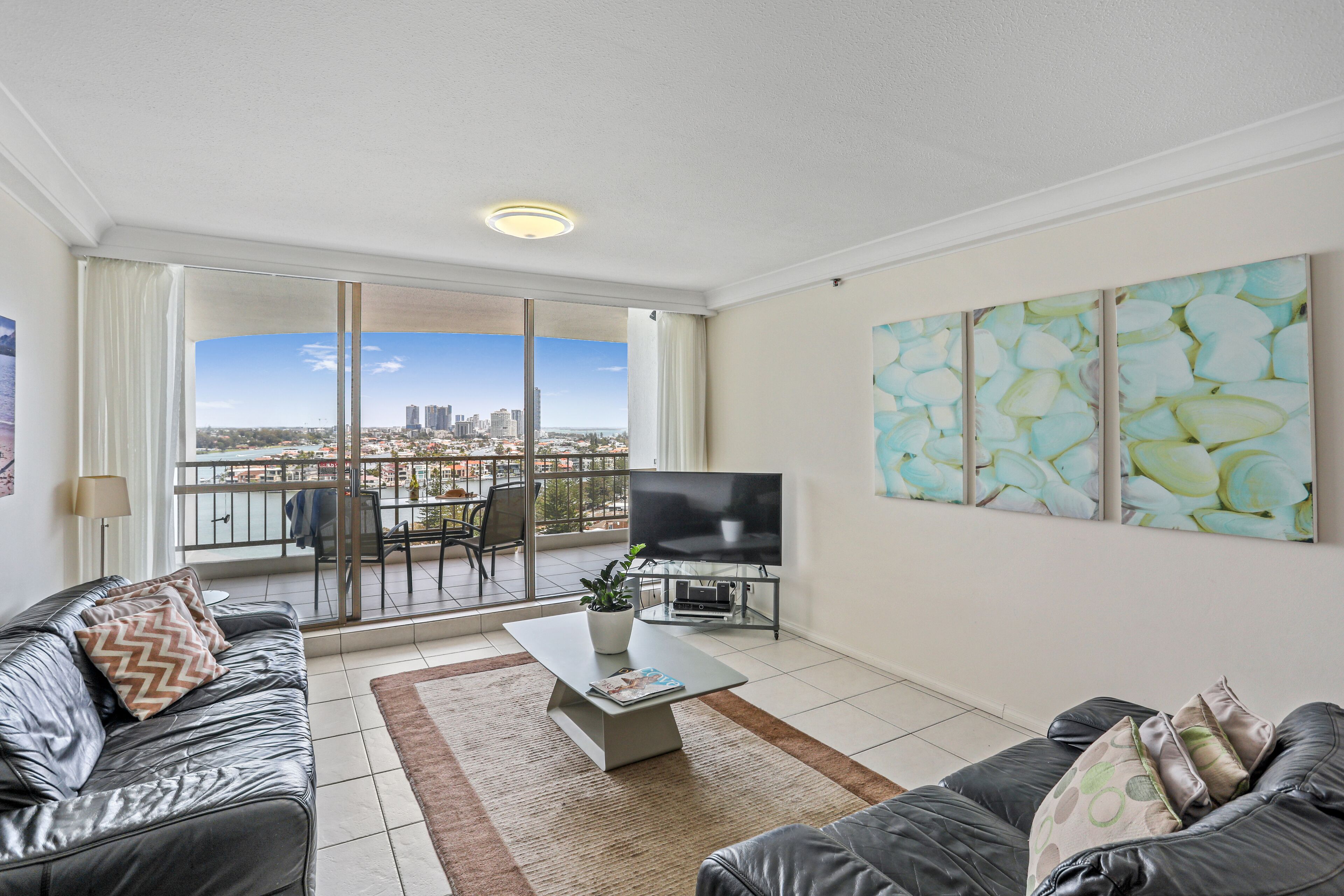A modern living room with a large window, a flat-screen TV, and a city view.