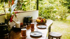 A wooden table with a fruit bowl, a toaster, and a vase with flowers.