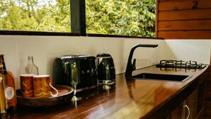 A kitchen with a wooden countertop, two stools, a sink, and a window with a view of greenery.