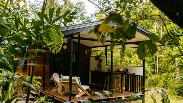 A wooden deck with two lounge chairs and a small table, surrounded by greenery.
