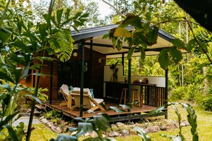 A wooden deck with two lounge chairs and a small table, surrounded by greenery. - Cape Trib Farmstay (Cape Tribulation)