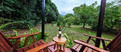 A wooden deck with two chairs and a small table, a bottle of wine, and a glass on the table.