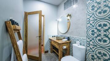 Un baño con tocador de madera, inodoro blanco, espejo y azulejos estampados.