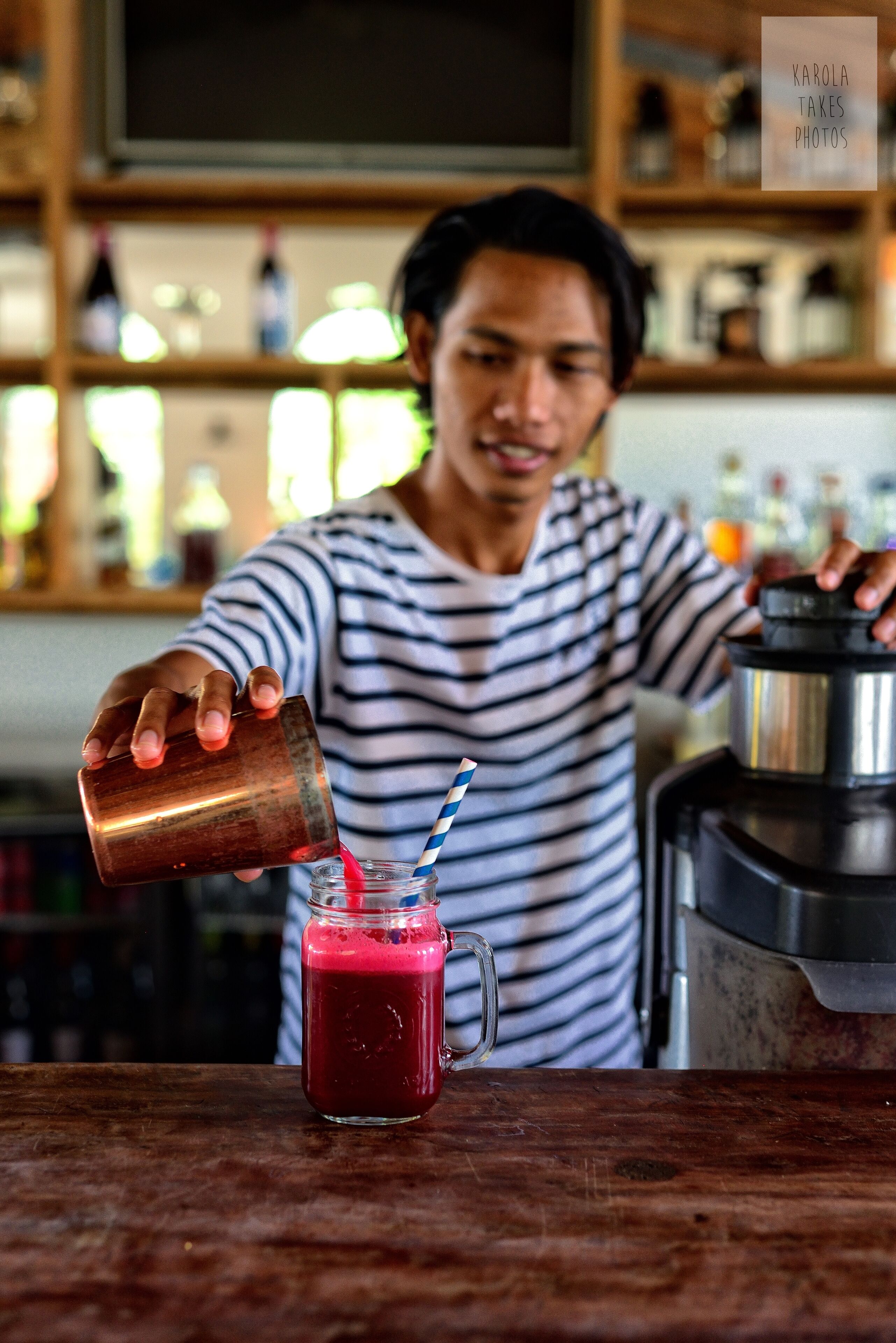 A person pouring a red beverage into a glass with a straw.