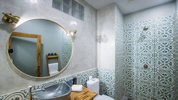 A bathroom with a round mirror, a wooden vanity, a stone sink, a toilet, and patterned tiles.