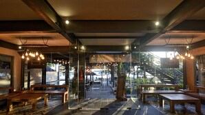 An indoor seating area with wooden benches and tables, a glass partition, and hanging light fixtures. - Trawangan Dive Centre (Gili Trawangan)