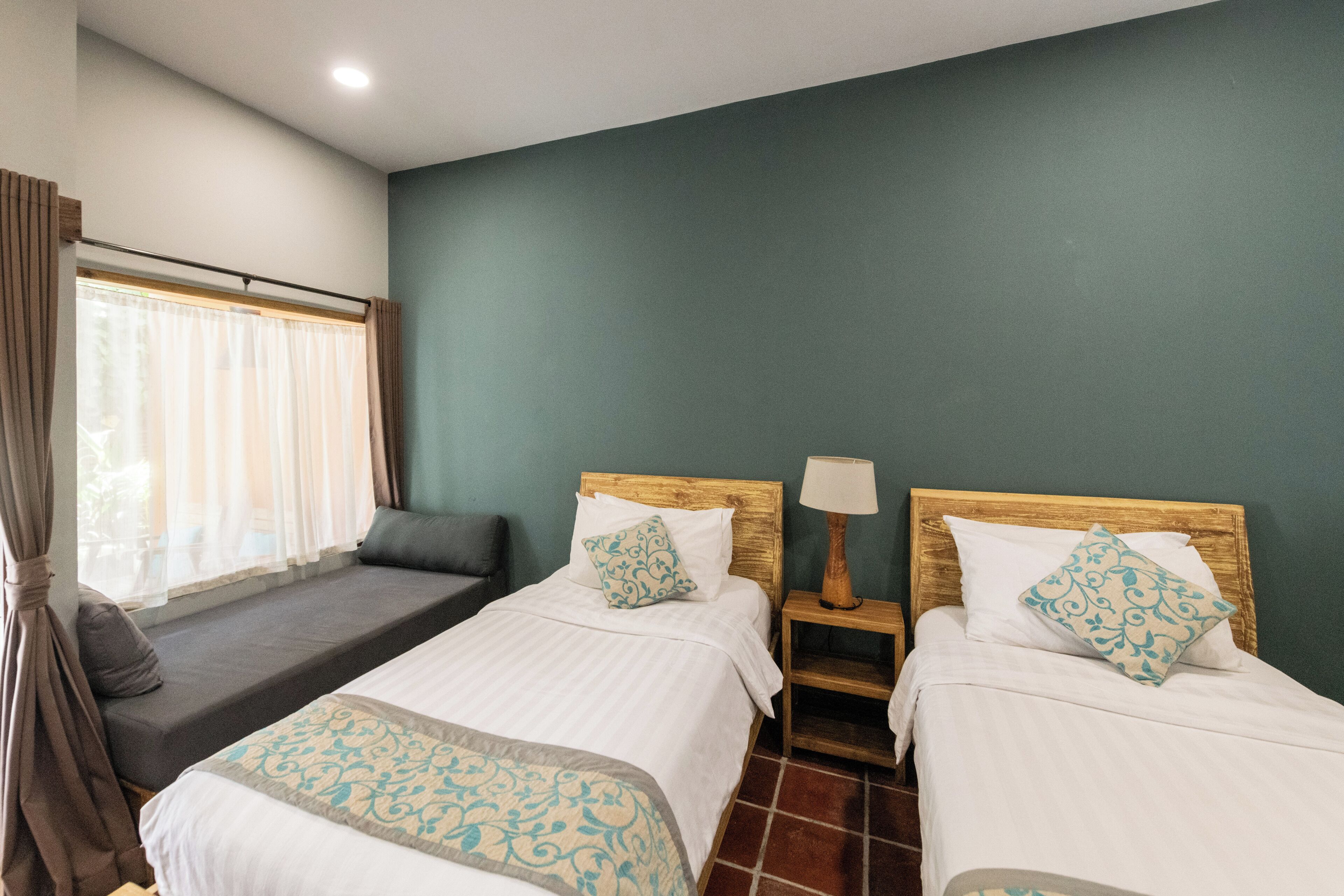 A hotel room with two beds, a bench, a nightstand, and a window with curtains.