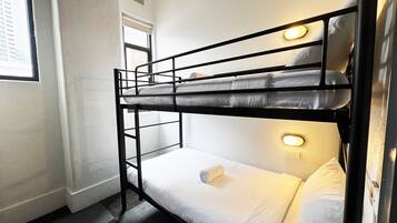 A bunk bed with two levels, a window with blinds, and a wall-mounted light fixture.