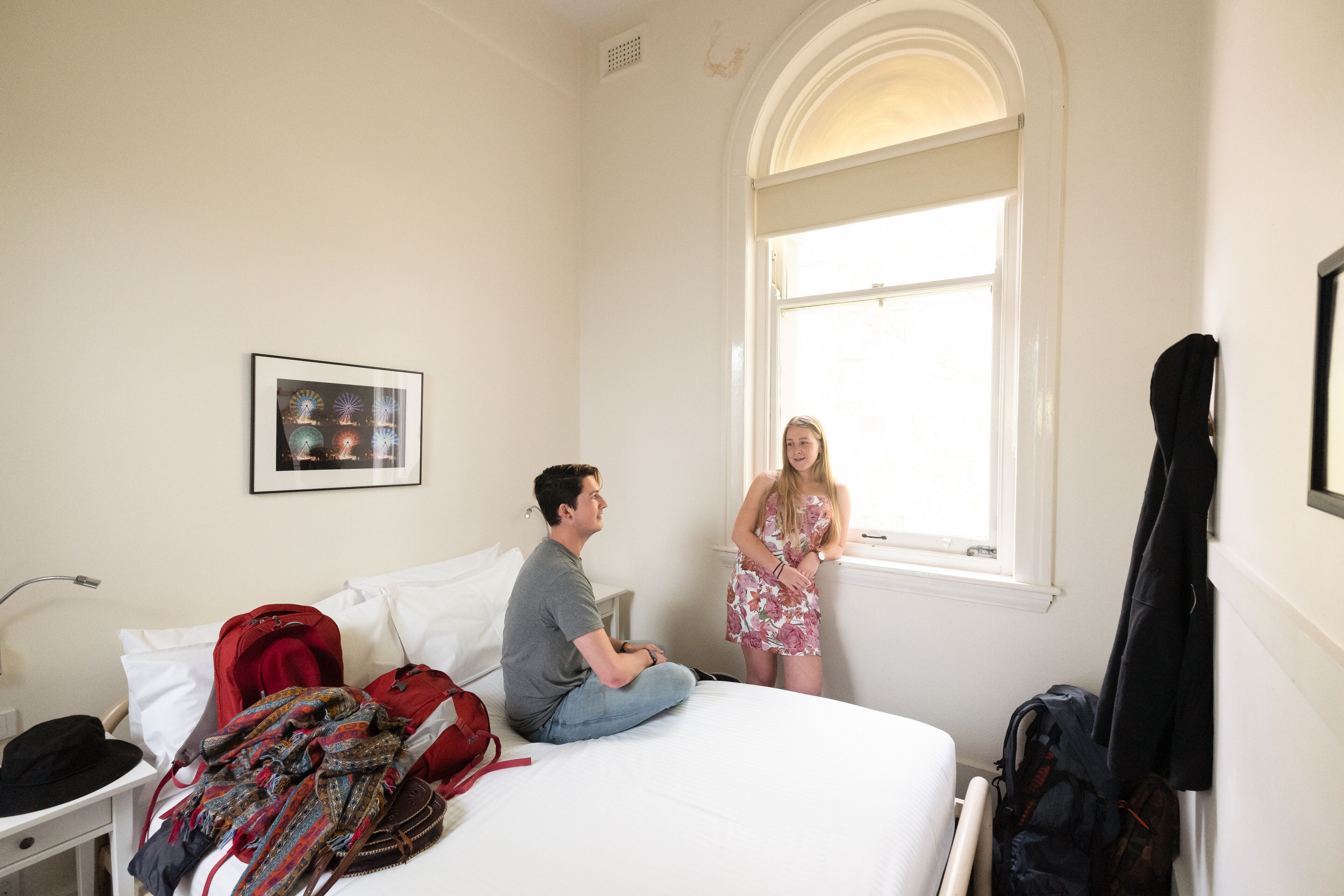 A hotel room with a bed, a window, a picture on the wall, and a guitar leaning against the wall.