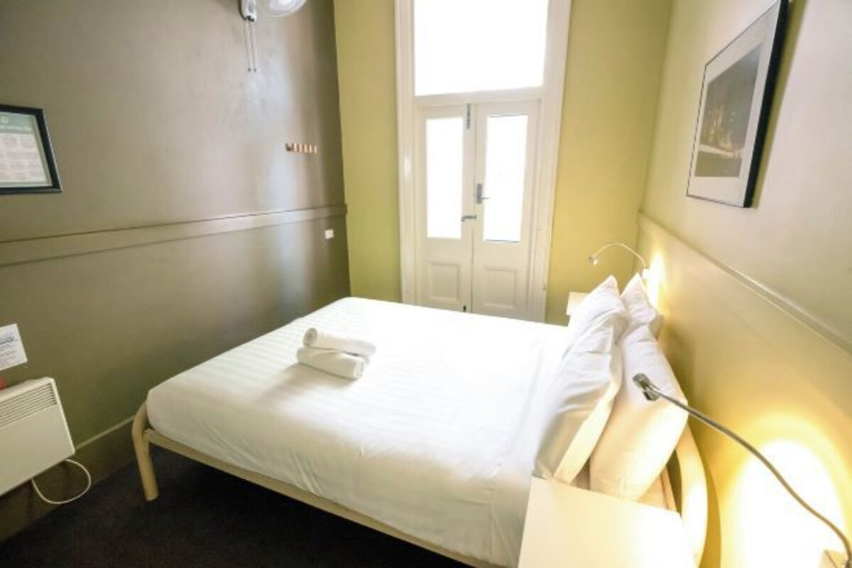 A single bed with white linens, a bedside lamp, and a framed picture on the wall.