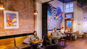 A cozy cafe with wooden benches and tables, a large mural on the wall, and a brick wall. - YHA Melbourne Central (Melbourne)