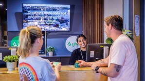 A reception desk with a television displaying a message about creating a more open and accommodating world. - YHA Melbourne Central (Melbourne)