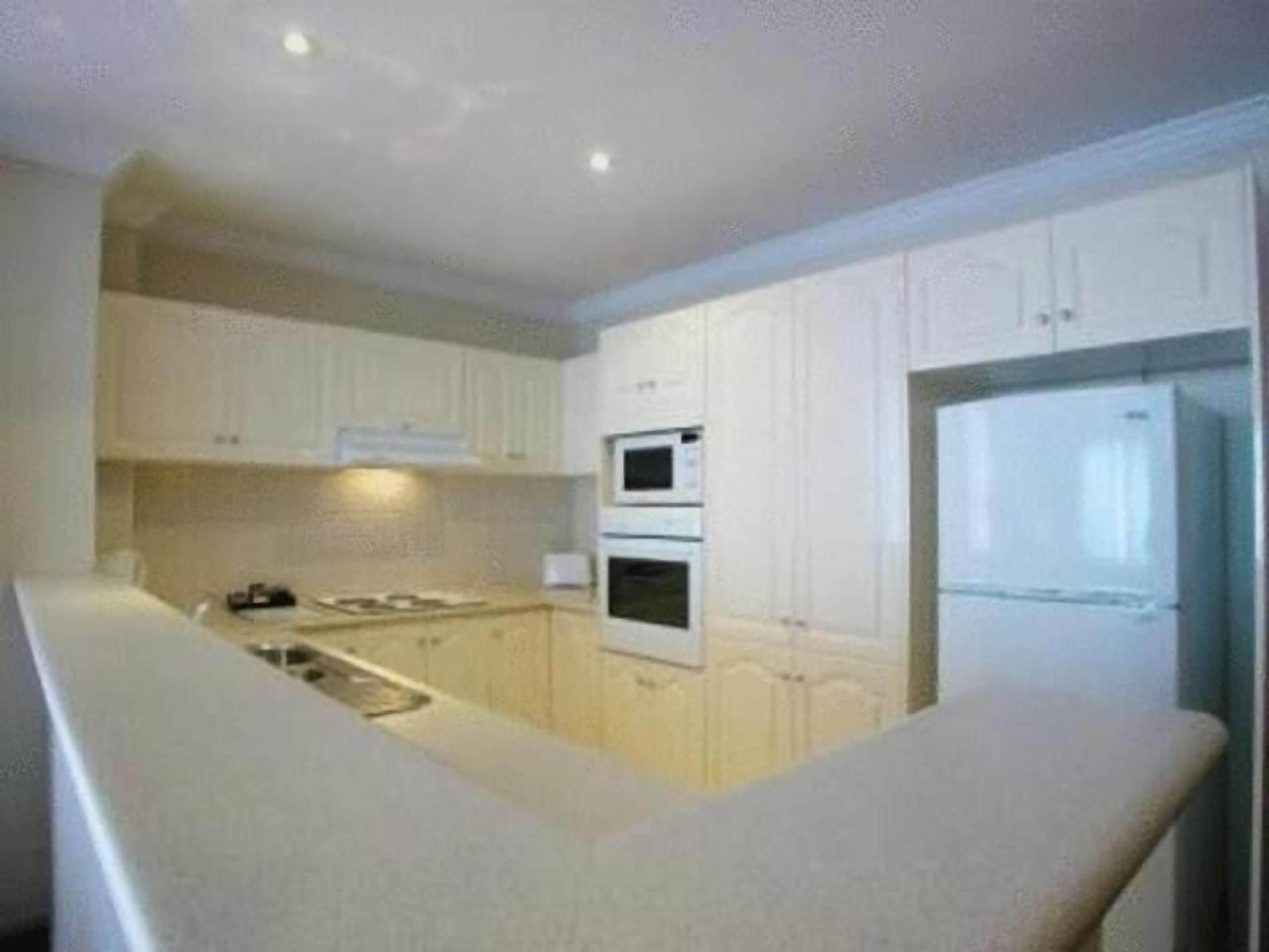 A compact kitchen with white cabinets, a built-in oven, and a refrigerator.