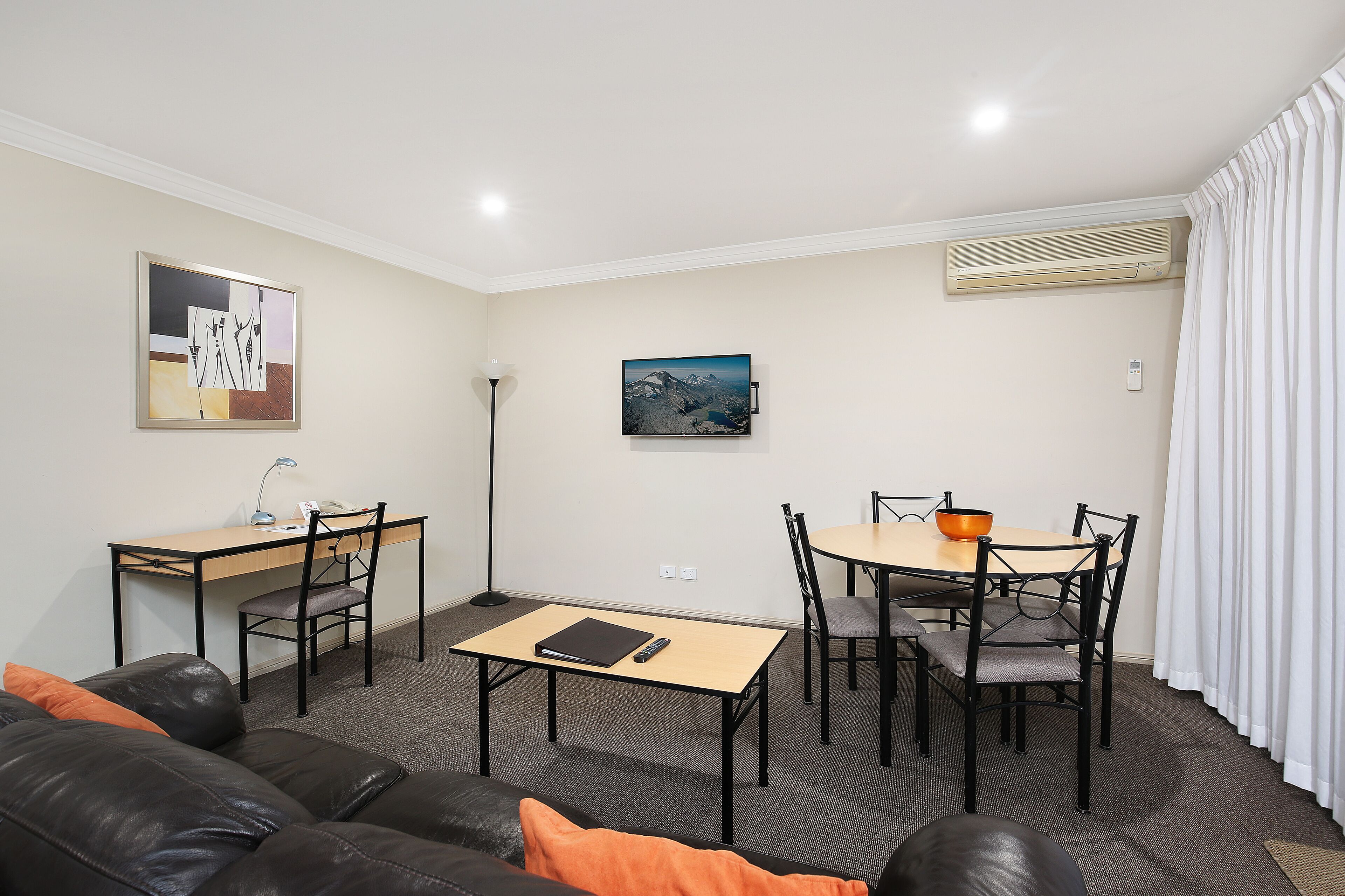 Una sala de estar moderna con un sofá, una mesa de comedor con sillas, un escritorio con una silla y obras de arte en las paredes.