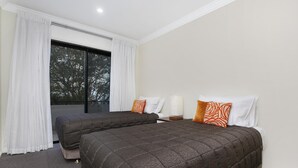 Een hotelkamer met twee bedden, witte gordijnen, een groot raam en uitzicht op bomen.