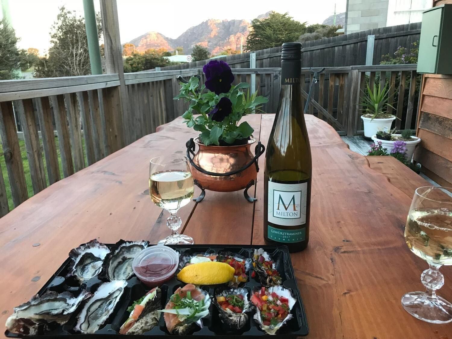 A wooden table with a bottle of wine, a glass, and a tray of oysters and seafood.