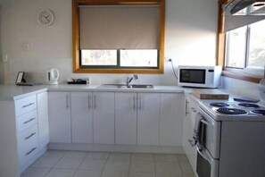 A kitchen with a sink, a microwave, a kettle, and a stove. - Gumnut Cottage (Coles Bay)