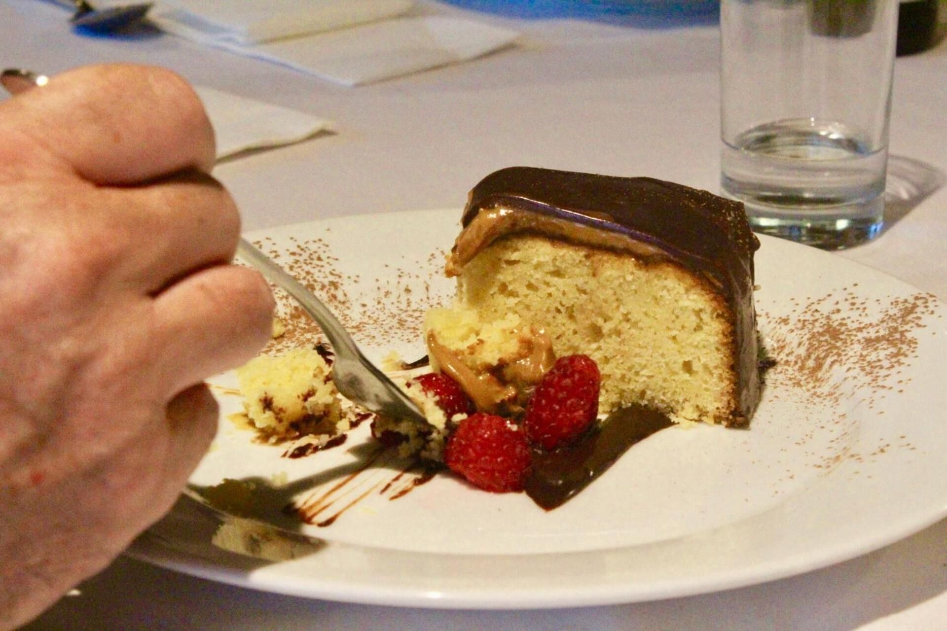 A slice of cake with chocolate topping, raspberries, and a fork.