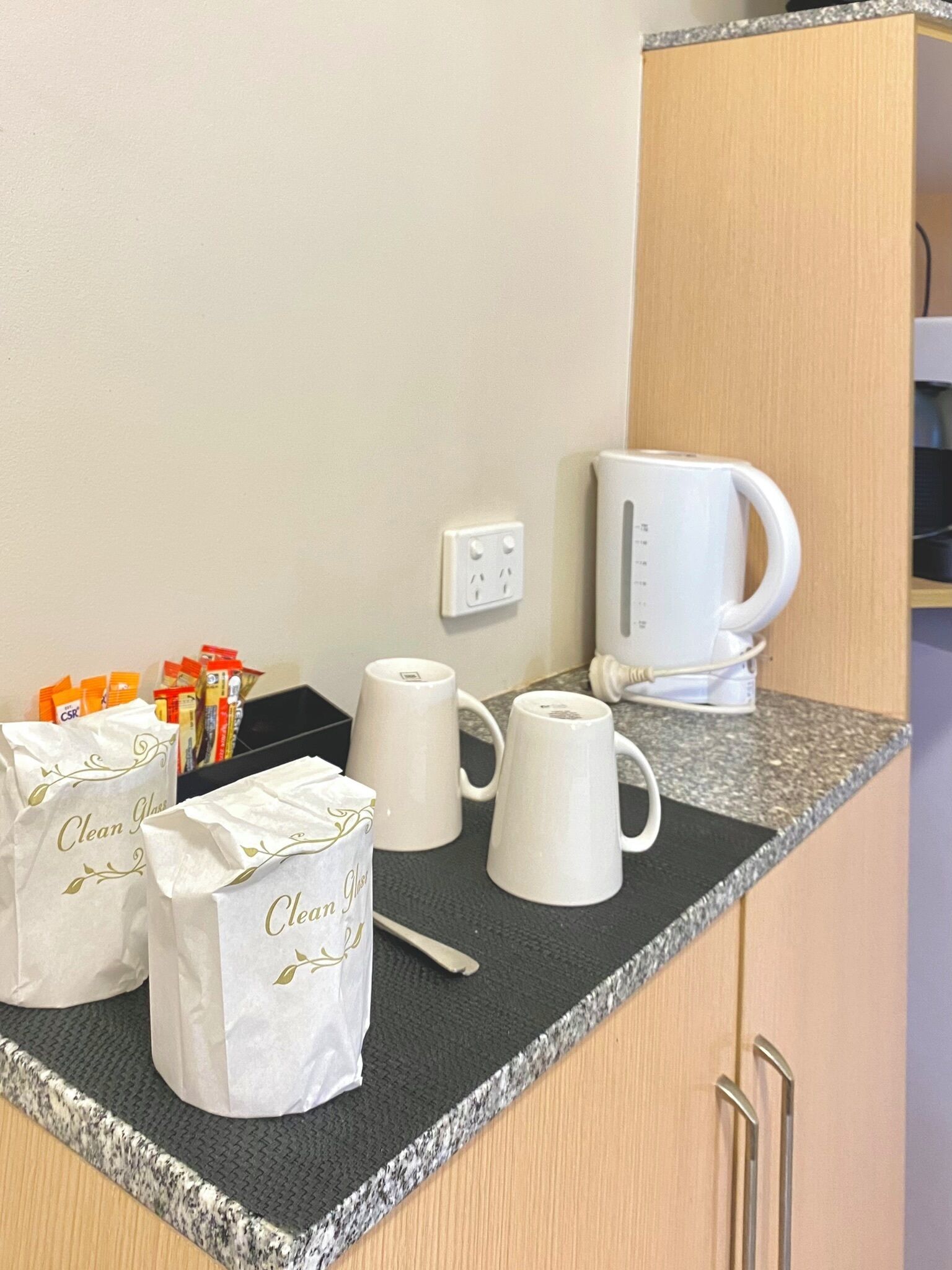 Un plan de travail de cuisine avec une machine à café, des tasses et des sacs étiquetés « Verres propres ».