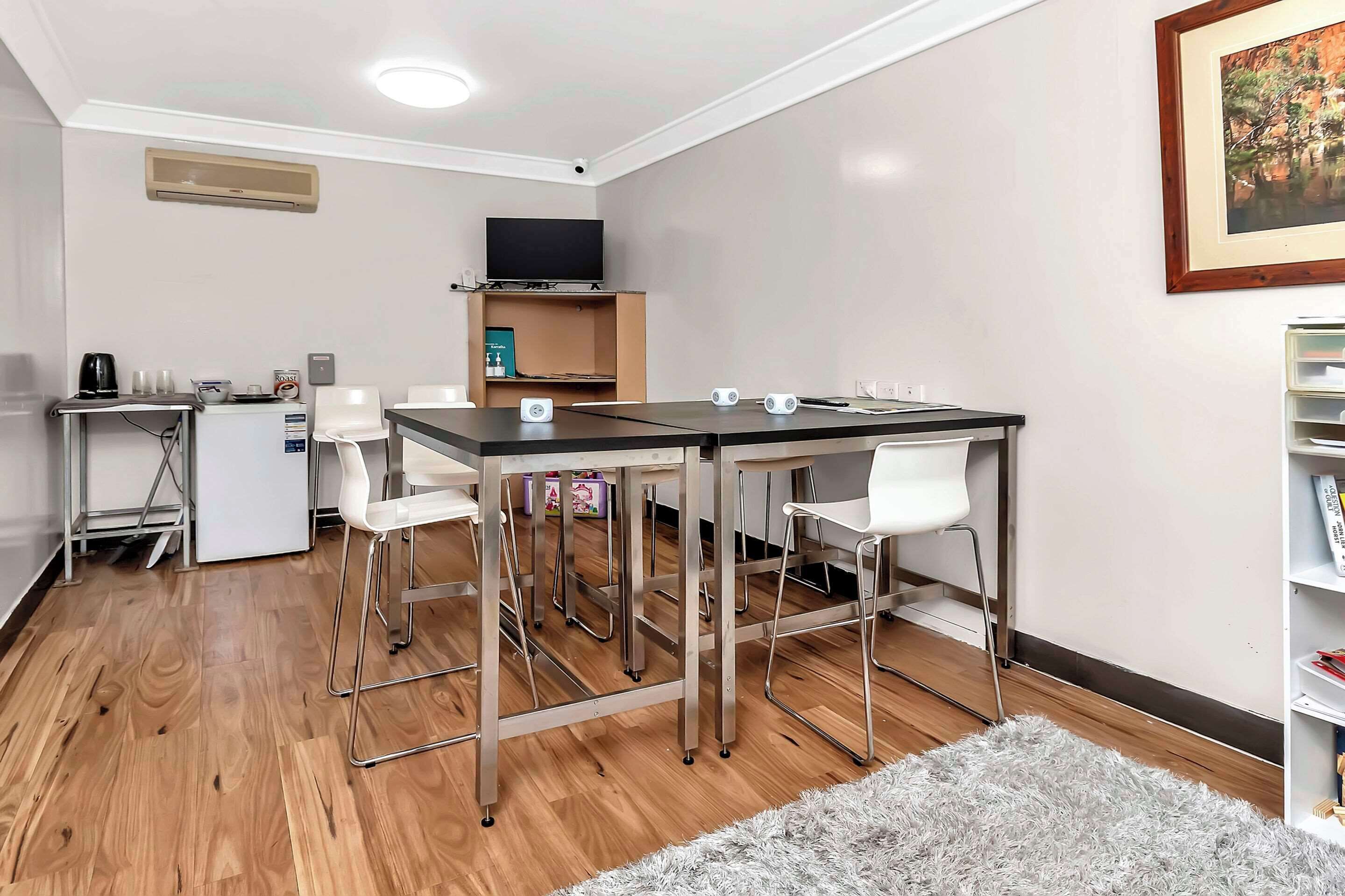 Una habitación moderna con una mesa de comedor, sillas, una pequeña kitchenette, un televisor de pantalla plana y una estantería.