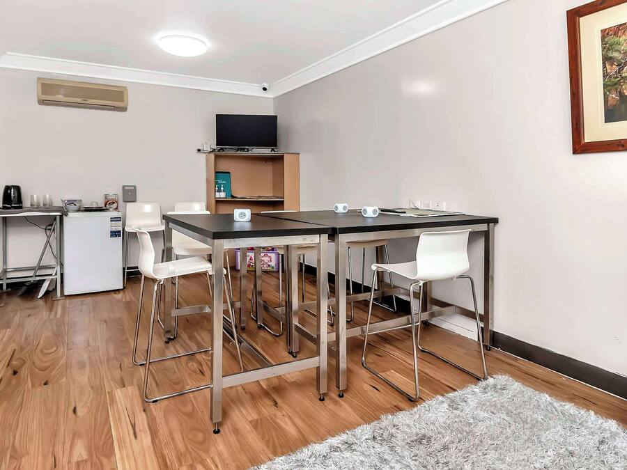 Una habitación moderna con una mesa de comedor, sillas, una pequeña kitchenette, un televisor de pantalla plana y una estantería.